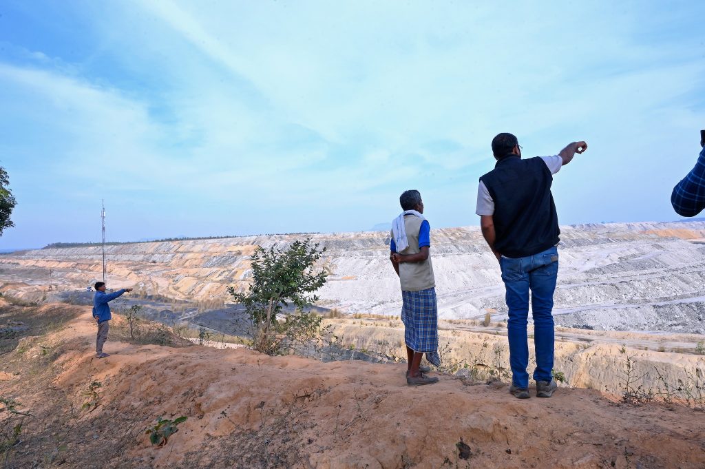 Alok and a couple of others stand on the edge of a giant mine site, with their backs to the camera as they stand on the edge of the pit.