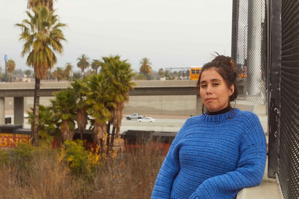 Photo of Andrea Vidaurre with a freeway and palm trees in the background.