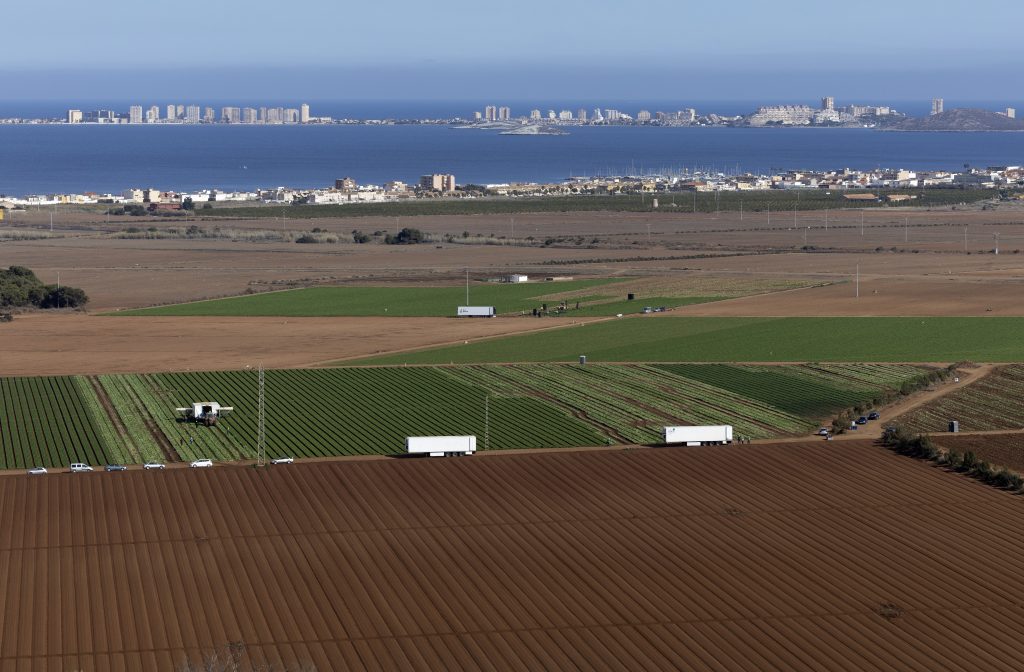 Photo of Mar Menor from a distance, showing agricultural fields close to the lagoon, with large residential buildings and hotels in the background 